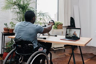 A man in a wheelchair using a handcycle exercising to a Kakana crosscycle class on his computer.