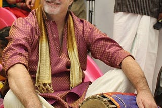 Me, sitting cross-legged with fancy clothes & a drum from India
