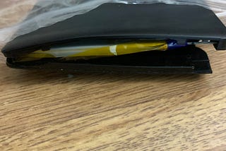 Color photo of a battery damaged by overheating under a simple light bulb. The insides are inflated and exposed, protruding from its case.