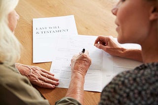 younger woman helping senior woman sign her last will and testament
