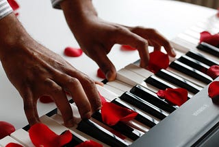 Brown hands playing a keyboard with rose petals scattered over it
