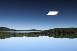 Upside-down image of a blue lake above a blue sky with a white raft seeming to hover in the sky.