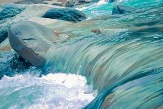 Close up shot of blue turquoise blue water flowing over smooth rocks