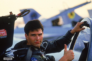 A fighter pilot, Tom Cruise, is behind the wheel in his plane and gives a thumbs up. Top Gun, Maverick, movie, film