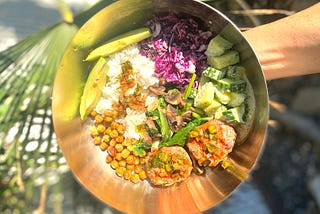 Bowl of fresh food including ahi tuna, avocados, kale, chickpeas, cucumber and purple cabbage.