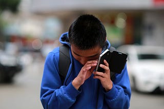 A blind man standing in the street, listening to his phone.