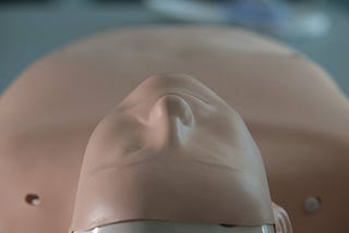 A CPR manikin lying face up on a grey floor