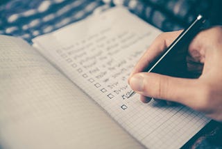 Notebook with checklist and hand holding pen to check things off