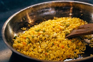 A metal bowl holds couscous with carrots and peas mixed in