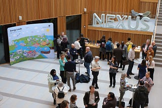 Aerial view of the reception space with people milling around small tables drinking coffee and networking. Energy Leeds banner in background.