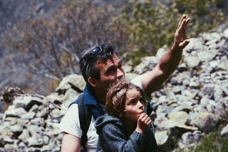 boy standing in front of a man in a rocky terrain during daytime