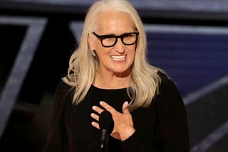 Jane Campion smiling at the podium, with her hand to her heart, as she gives her acceptance speech for Best Director at the 2022 Oscars.