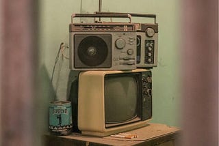 A grainy photograph of a transistor radio sitting atop an old television in a run-down room.