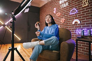 Woman sitting in front of a ringlight in a chair talking to a phone camera.