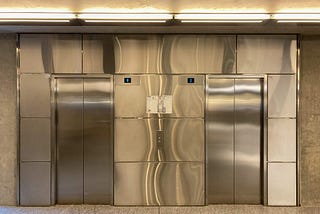 Two stainless steel elevator doors on a shiny metal wall