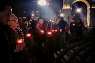 Students and faculty in front of the arch at Washington Square Park at night, holding candles.