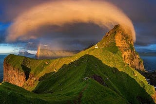 a rainbow peeks from under a billowing cloud arcs across a craggy mountain range