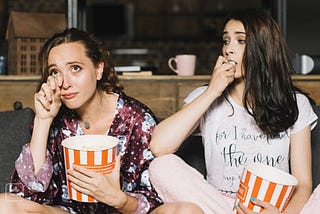Women (on the left) cries while watching a movie, while her friend (on the right) watches her with concern.