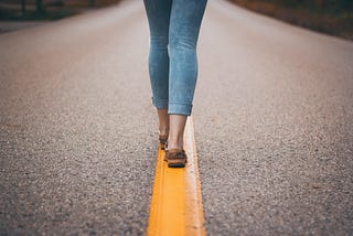 A woman walking a yellow line on a highway