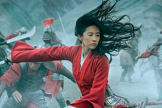 Promo image from Disney’s live action Mulan: Mulan in a red dress with her hair flying, in battle.