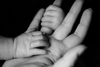 Black and white photo of baby gripping mother’s finger