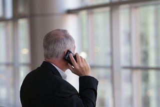 A grey-haired man in a suit talks on telephone.