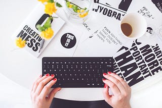 What You Need to Know Before You Start Blogging — Blogging Tips. Post by David Mania (www.davidmania.com). This image displays a woman typing on a black keyboard with posters and a coffee on the table beside the keyboard.