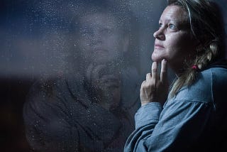 Clear glass window panel casting reflection of woman with hand touching jaw