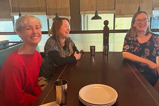 Three women sitting at a restaurant table, smiling