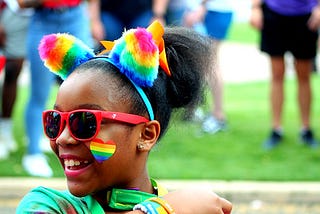 Young girl of colour at a pride parade wearing rainbow accessories and smiling