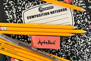 Black and white composition notebook with pencils, pen, eraser and red folder