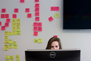 Person sitting behind a computer monitor in front of a wall of post-its