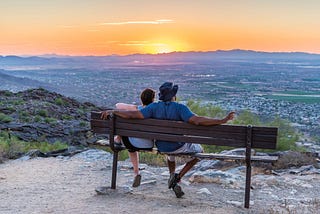 Two people sitting on a bench looking at the sunset.