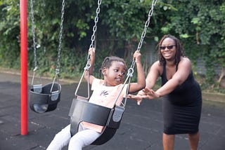 Child on a swing being pushed by a smiling woman, showing patience and right timing.