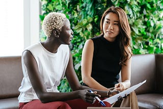 Two women sit next to one another referring to a piece of paper.