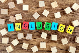 An image of the word inclusion spelled out on a table with different color blocks surrounded by wooden blocks