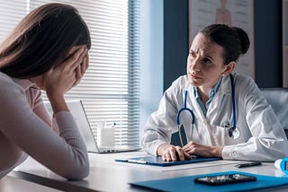 Sad woman with her head in her hands sitting across from a doctor.