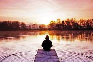 Silhouette of a person sitting on a dock, reflecting upon a wilderness sunrise.