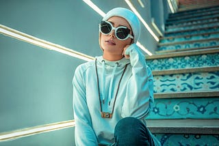 A woman wearing sunglasses sitting on a stair case.