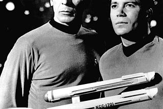 Vintage black and white photo of Captain Kirk and Mister Spock from Star Trek TOS with a model of the star-ship Enterprise in the foreground. Source Wikimedia Commons.