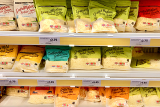 Various coloured packets of grated cheese lined up on supermarket shelves.