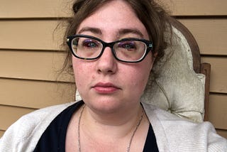 A late twenties woman with glasses and bruised eyes.