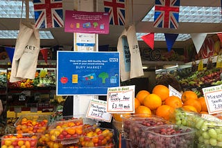 A fruit and veg stall at Bury Market with a sign saying “shop with your NHS Healthy Start card at your award-winning Bury Market”