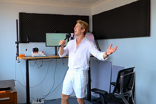 extravagant man in all white linen singing in front a computer monitor