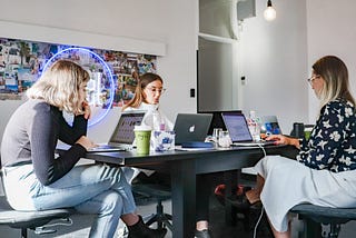 Three women sit around a table working intently on laptops