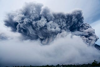 A volcano amongst the clouds erupting a blast of smoke in a cool blue lighting.