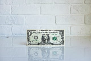 A single dollar bill in front of a white brick wall