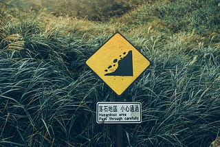 A warning sign showing tumbling rocks and the written notice ‘hazardous area. Pass through carefully’