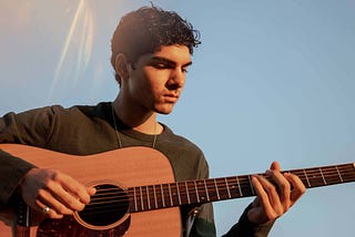 Young man playing guitar under clear, blue sky