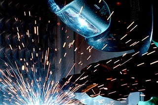 A person in protective gear welding a metal bar.